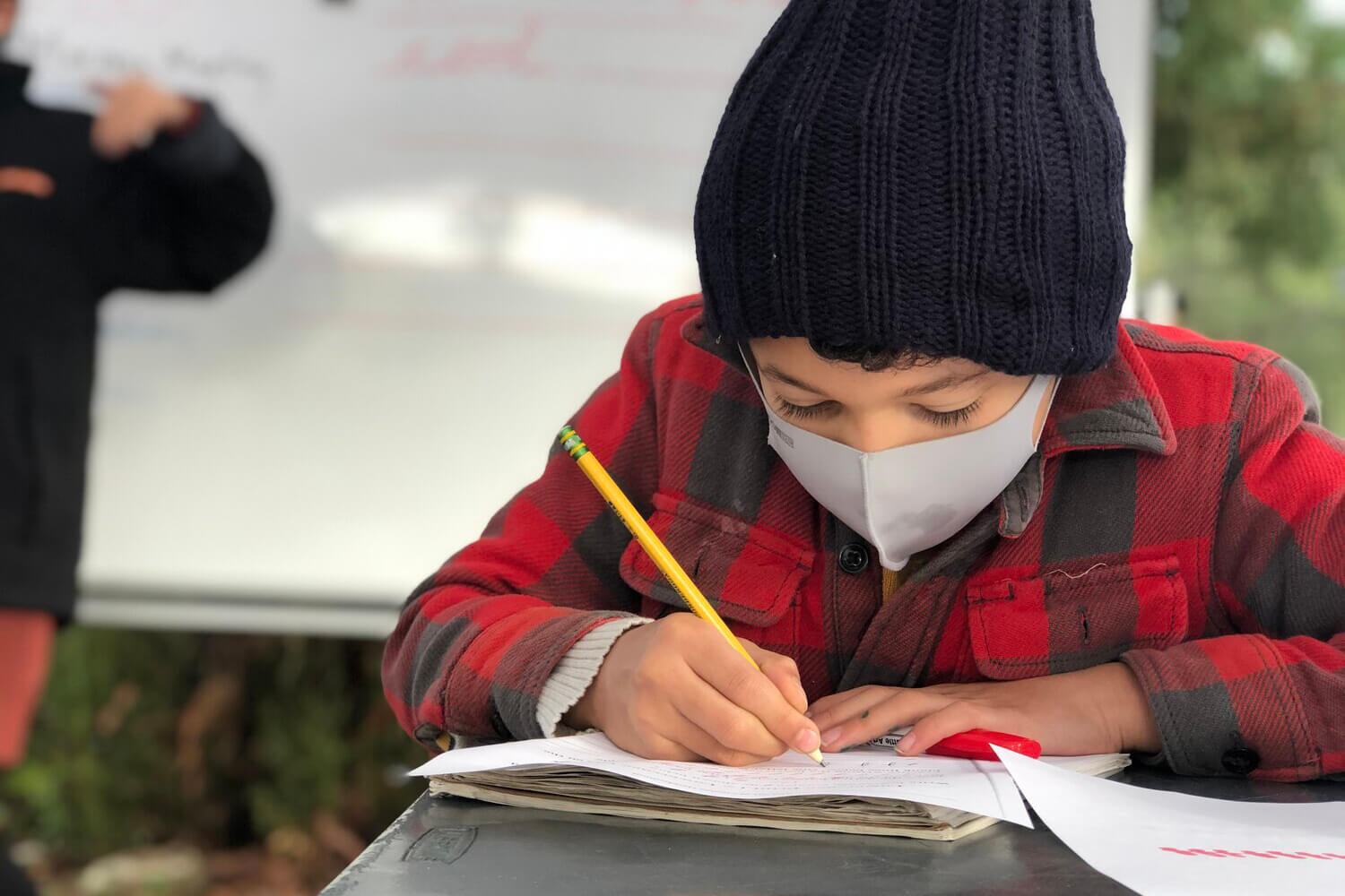 Boy with a face mask writing in a notebook.