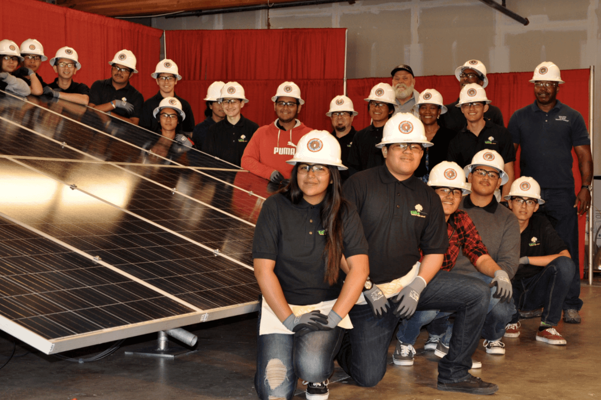 Students wearing hard hats standing next to solar panels